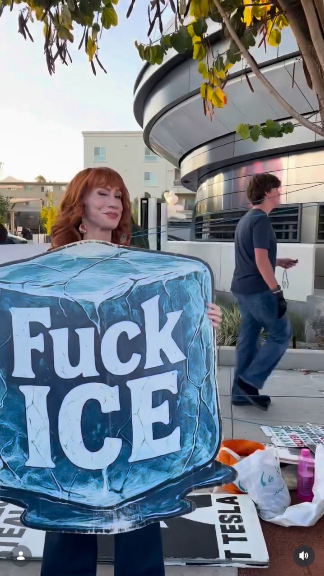 Kathy Griggin is standing outside the Tesla Diner with a bunch of other protesters (who are mostly out of this frame). She's holding a big sign painted like a blue ice cube that says "Fuck ICE."