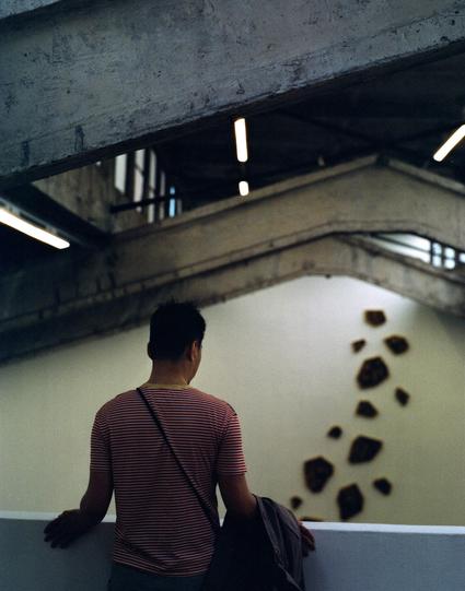 Harman Phoenix 200 II (6x7)

##English
A person with a red-and-white striped shirt and a striped bag stands under a concrete structure. In front of them, a series of dark, irregularly shaped objects appear to be on a pale wall.
##中文
一名穿着红白条纹衫、背着挎包的人站在一个混凝土结构下。前方有一系列不规则形状的深色物体，看起来在浅色墙面上。
