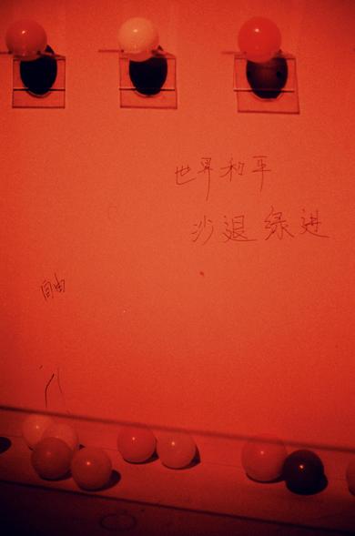 Harman Red 125 (FF)

English
A red-lit wall with three circular light fixtures, each containing a bulb. The bulbs are red, white, and red from left to right. Below the fixtures, Chinese characters are written in white: "世界和平 沙退绿进" (World Peace, Dunes Make Way For The Greens). Additional smaller lights are visible at the bottom of the image.
中文
一面红色灯光照亮的墙壁，上方有三个圆形灯具，每个灯具内有一个灯泡。从左到右灯泡的颜色依次为红色、白色、红色。灯具下方用白色书写着中文字：“世界和平 沙退绿进”。图片底部还可以看到更多小灯光。