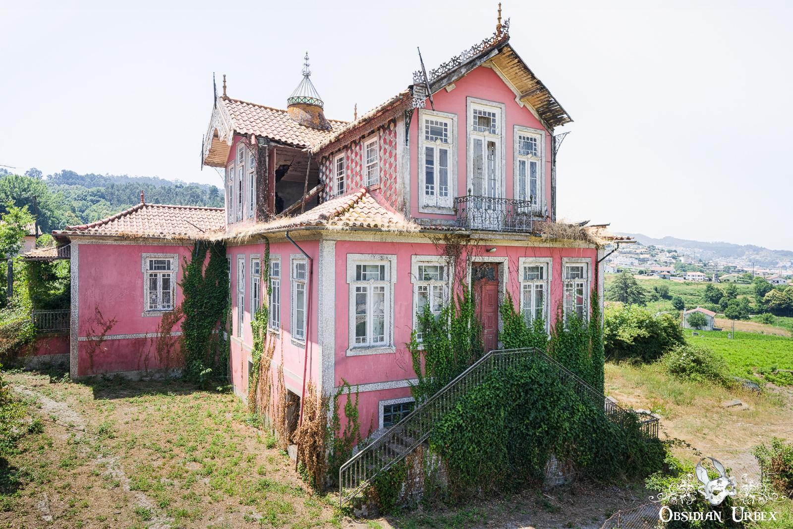 An abandoned ornate pink mansion, partially overgrown with ivy, stands in a rural landscape. I
