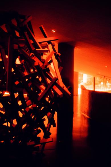 Harman Red 125 (FF)

English
A close-up of a chaotic, abstract sculpture made of intersecting wooden or metallic beams. The beams are arranged in sharp, angular shapes, creating a dense and intricate structure. The background is dark, with a warm orange glow illuminating the sculpture from the right side, casting dramatic shadows.
中文
一个由交错的木质或金属梁组成的混乱、抽象雕塑的特写。这些梁以尖锐的角度排列，形成一个密集而复杂的结构。背景昏暗，右侧有一束温暖的橙色光线照亮雕塑，投射出戏剧性的阴影。