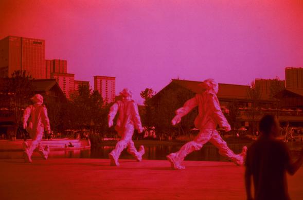 Harman Red 125 (FF)

##English
A red-toned image of a cityscape at dusk or night. Three human-shaped statues in are placed in a line across an open plaza, with one person close to the foreground, blurred due to the depth of field. The background features tall buildings and trees, all bathed in a deep red hue. The scene appears to be in an urban park or public space.
##中文
一张黄昏或夜晚的城市景观红色调图像。三个人形雕塑横排成一列在一个开放的广场。前景中是一个因为景深而略微模糊的人。背景中有高楼和树木，所有景物都浸润在深红色调中。场景看起来是在城市公园或公共空间。