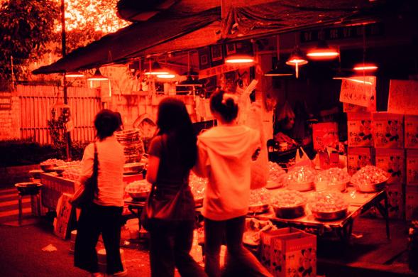 Harman Red 125 (FF)

English
A red-toned photograph of a bustling night market stall. Three people are visible. The stall is lit by bright lights and displays various food items, including stacked bowls and bags of snacks. Chinese characters are visible on signs and boxes.
中文
一张红色调的夜市摊位照片。照片中有三个人。摊位被明亮的灯光照亮，展示着各种食物，包括叠放的碗和零食袋。中文字样出现在招牌和箱子上。