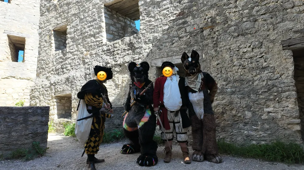 Two Landsknechts, a Jaguar fursuiter and a Blue Heeler fursuiter in a group photo. One of the Landsknechts and the Jaguar fursuiter brandish spears, while the second Landsknecht holds a sword.