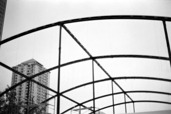 Fujifilm NEOPAN F (FF)

English
A black-and-white photograph of a curved metal framework structure in the foreground, with a tall, modern high-rise building visible in the background. The metal framework consists of intersecting arches, and the building has a grid-like facade with numerous windows.
中文
一张黑白照片，前景是一个弯曲的金属框架结构，背景中可见一座高大的现代摩天大楼。金属框架由相交的拱形组成，大楼的外墙呈网格状，有众多窗户。