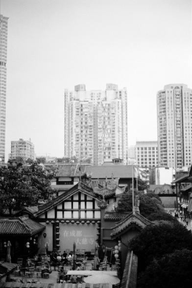 Fujifilm NEOPAN F (FF)

English
A black-and-white photograph of a traditional Chinese building with a tiled roof and intricate architectural details. In the background, modern high-rise buildings rise above the traditional structure. The foreground includes outdoor seating and tables, possibly part of a café or restaurant. A sign with Chinese characters is visible on the traditional building.
中文
一张黑白照片，展示了一幢传统中式建筑，屋顶铺有瓦片，建筑细节精美。背景中，现代高层建筑耸立在传统建筑之上。前景有户外座椅和桌子，可能属于咖啡馆或餐厅。传统建筑上可见中文字样的标志。