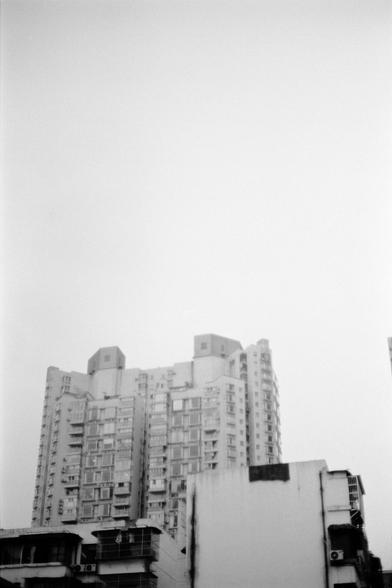 Fujifilm NEOPAN F (FF)

English
A black-and-white photograph of a tall residential building. The building has multiple floors with balconies and air conditioning units attached to the exterior. The sky above is bright and clear, creating a stark contrast with the building. The lower part of the image shows rooftops of adjacent structures.
中文
一张黑白照片，拍摄了一幢高层住宅楼。楼房有多层，每层都有阳台和外墙上的空调设备。上方的天空明亮清朗，与建筑形成鲜明对比。图像下方显示了相邻建筑的屋顶。