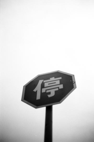 Fujifilm NEOPAN F (FF)

##English
A black-and-white image of an octagonal stop sign with the Chinese character "停" (meaning "stop") in white text on a dark background. The sign is slightly tilted and mounted on a pole.
##中文
一张黑白照片，显示一个八边形的停车标志，黑色背景上有一个白色的“停”字。标志略微倾斜，固定在一根杆子上。