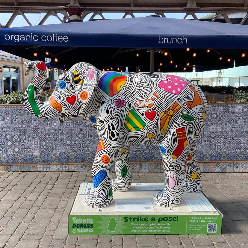In a pedestrianised street, a fibreglass sculpture of an elephant.

It's colourfully decorated with a design that includes hearts, flowers, and for some reason socks and underpants.