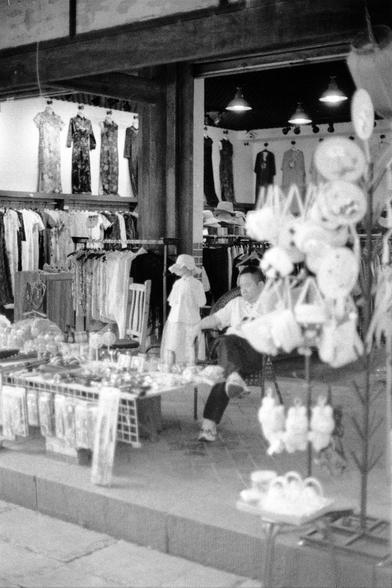 Lucky LUCKY SHD 400 (FF)

English
A black-and-white photograph of a clothing store interior. The shop is filled with racks of traditional dresses and garments, displayed on mannequins and hangers. A person is seated on a chair in the background, partially obscured by the clothing. The foreground features tables with various items, possibly accessories or decorative objects. The store has a rustic, wooden structure, and hanging lights illuminate the space.
中文
一张黑白照片，展示了一家服装店的内部。店内摆满了传统连衣裙和服装，陈列在…