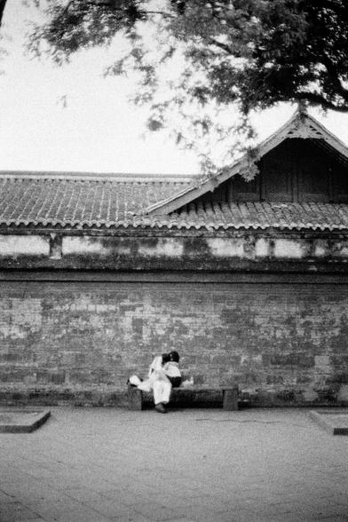 Lucky LUCKY SHD 400 (FF)

English
Black-and-white photograph of a traditional building with a tiled roof and white walls. Two people sit on a stone bench against the wall, facing away from the camera, hugging each other. The wall is made of large, rectangular bricks, and the roof has curved eaves. Tree branches hang into the frame from the top left, adding a natural element to the architectural scene.
中文
黑白照片，展现了一座传统建筑，屋顶铺着瓦片，墙壁为白色。两人坐在石凳上，背对着镜头，靠在墙上，拥抱着彼此。墙由大块长方形砖块砌成，屋顶有弯曲的屋檐。左上角有树枝伸入画面，为建筑场景增…