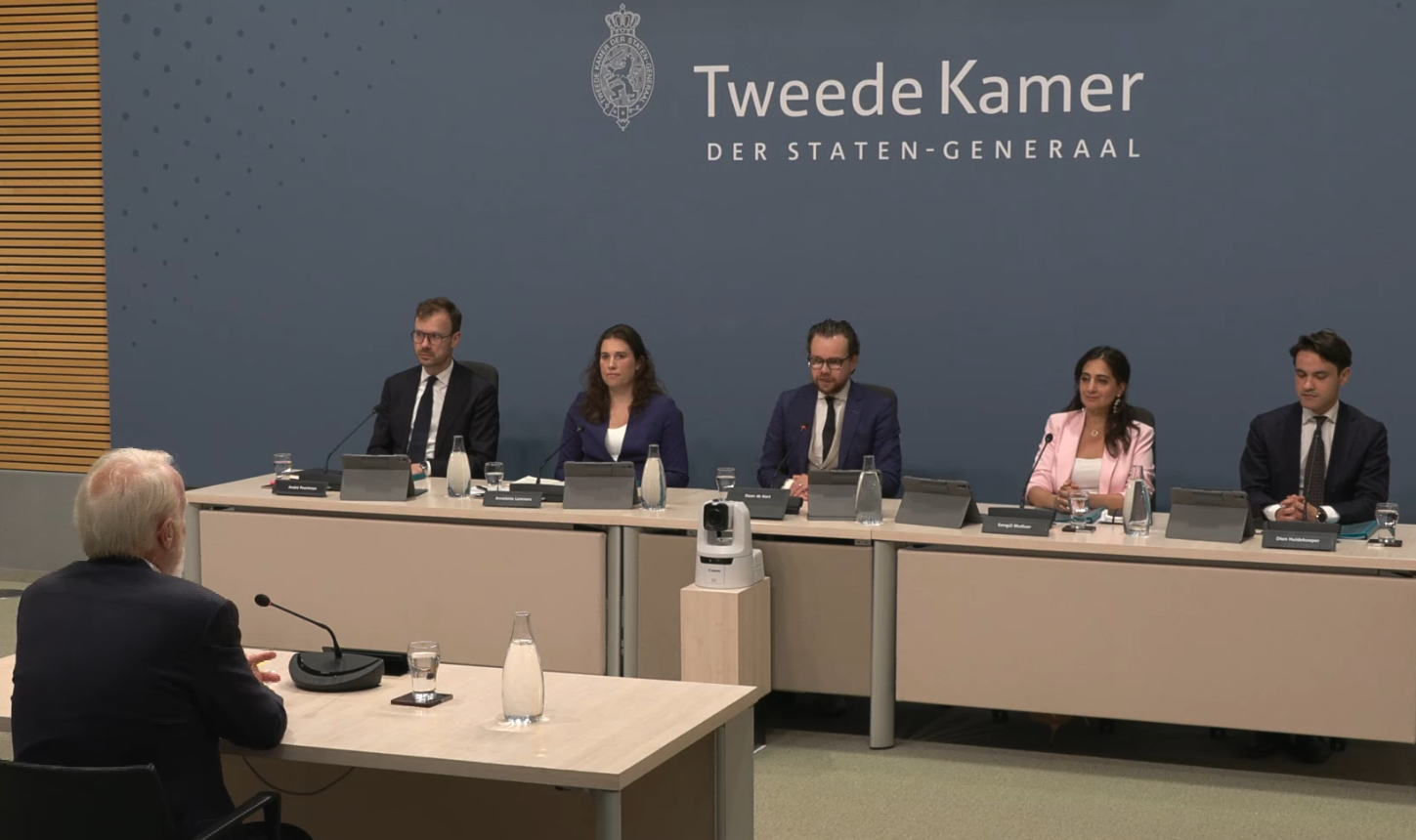 Parlementaire Enquêtecommissie Corona, verhoorweek 5, 1 juli 2026 om 15:00 uur: Jaap van Dissel, destijds voorzitter van het OMT en het RIVM, wordt voor de tweede keer verhoord door de enquêtecommissie. De commissieleden van links naar rechts: André Poortman (CDA), Annelotte Lammers (Groep Markuszower), Daan de Kort (VVD, voorzitter), Songül Mutluer (PRO, ondervoorzitter) en Dion Huidekooper (D66). De twee eerstgenoemden doen het belangrijkste deel van deze ondervraging. Links vooraan kijken we Jaap van Dissel op de rug, hij zit tegenover de commissie.