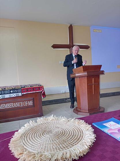 Man behind a lectern with a cross.