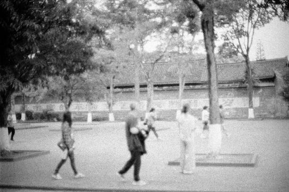 Lucky LUCKY SHD 400 (FF)

##English
A black-and-white, slightly blurred photograph of a group of people walking in an open area. The background features a traditional building with a tiled roof, partially obscured by trees. The people appear to be engaged in casual activities, and the overall scene suggests a park or a public space with a cultural or historical setting.
##中文
一张略显模糊的黑白照片，展示了一群人在开放区域行走。背景是一座传统建筑，屋顶铺有瓦片，部分被树木遮挡。人们看起来在从事休闲活动，整个场景暗示这是一个公园或具有文化或历史意义的公共空间。
