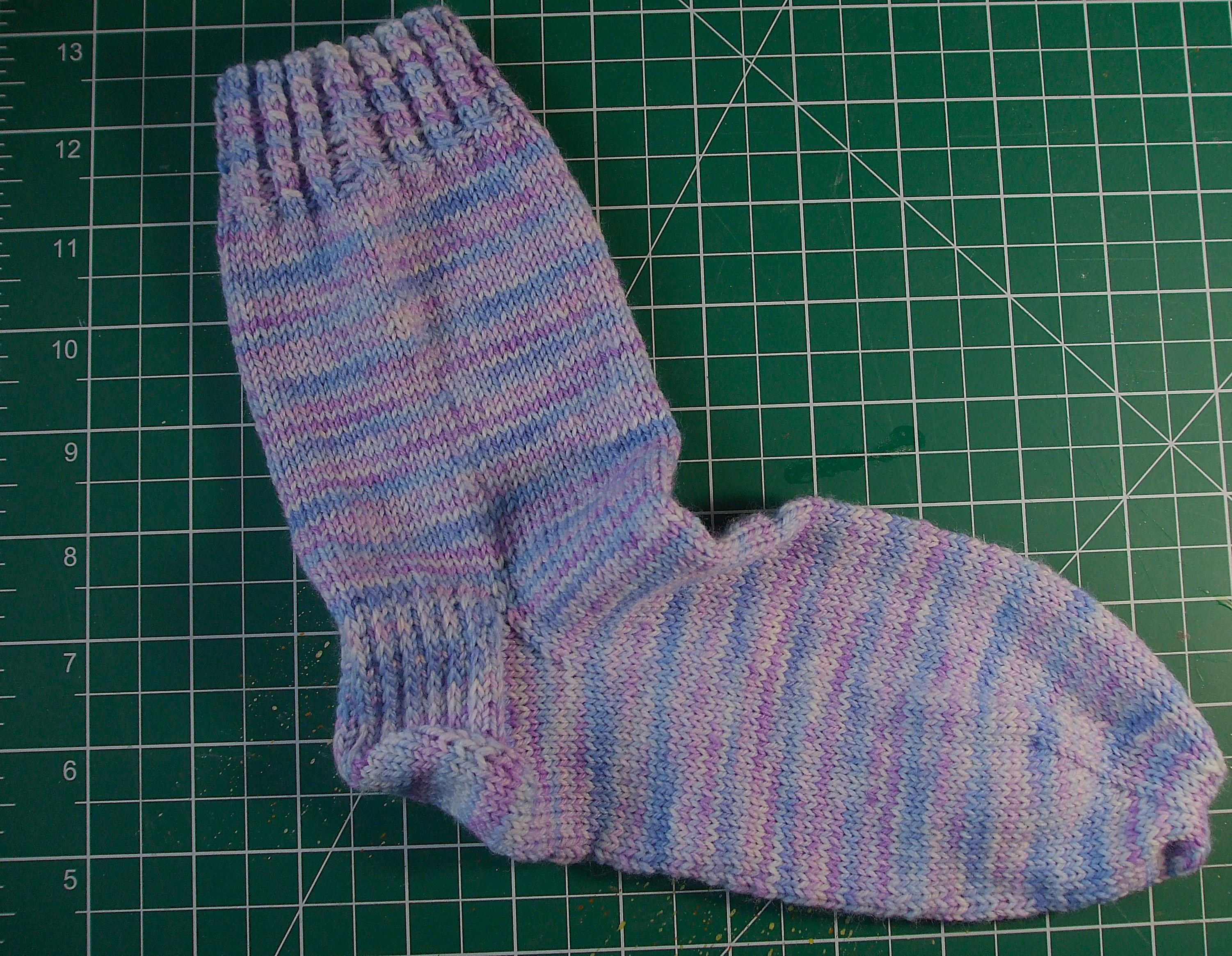 Hand knit sock in variegated yarn in pale blues, purples and pinks, all the hydrangea colours, with a fake cable ribbing.