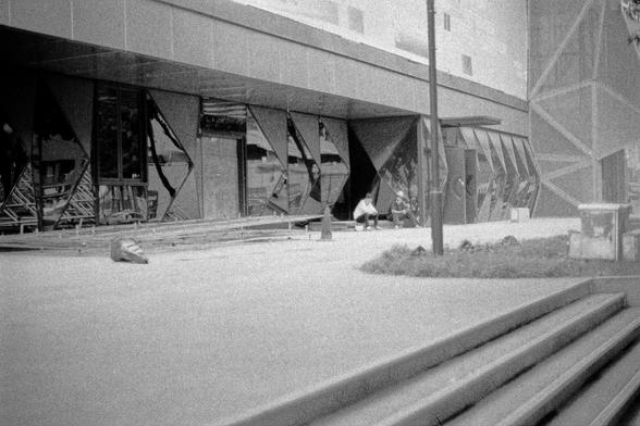 Lucky LUCKY SHD 400 (FF)

English
A black-and-white photograph of a site. The image shows a large building with a modern, geometric facade featuring triangular and rectangular glass panels. Two individuals are seated on the ground near the entrance, which is surrounded by scaffolding and construction materials. The ground appears to be concrete, and there are steps leading up to the building. The scene is quiet, with no active construction visible.
中文
一张黑白照片，展示了一个工地。图像中有一栋大楼，其外立面采用现代几何设计，有三角形和矩…