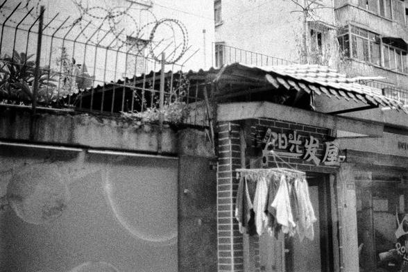 Lucky LUCKY SHD 400 (FF)

English
A black-and-white street scene showing a building with a tiled roof and a sign in Chinese characters, likely a barbershop or salon. Towels are hanging on a line outside the shop. Above, there is a fence topped with barbed wire and some vegetation.
中文
一张黑白的街道场景照片，展示了一栋带有瓦片屋顶的建筑，上面有一个中文字符标志，可能是一家理发店或美容院。店外挂着晾晒的毛巾。上方有一个带铁丝网的围栏和一些植被。