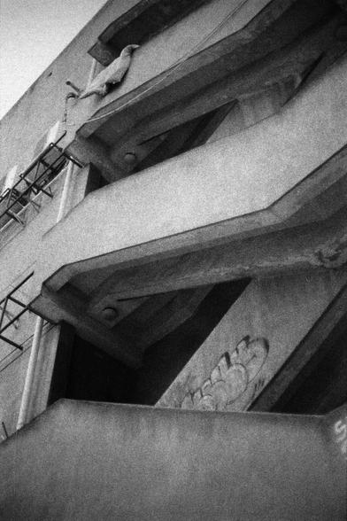 Lucky LUCKY SHD 400 (FF)

A black-and-white photograph of a quilt hanging on a concrete ledge of a multi-story building. The building features angular architectural lines, scaffolding on the left side, and a carved or sculpted design on the lower right section. The quilt is positioned near the top left corner of the ledge, facing left.
中文
一张黑白照片，展示了一条被子晾在一栋多层建筑的混凝土窗台上。建筑物具有尖锐的建筑线条，左侧有脚手架，右下角有一个雕刻或雕塑的设计。被子位于窗台的左上角附近，面向左侧。