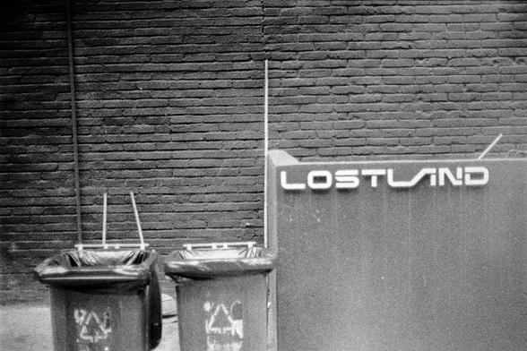 Lucky LUCKY SHD 400 (FF)

English
A black-and-white photograph of a brick wall with two trash bins placed against it. The word "LOSTLAND" is prominently displayed in large, bold letters on a sign or structure to the right of the trash bins. The trash bins have recycling symbols on their sides.
中文
一张黑白照片，展示了一面砖墙，前面放着两个垃圾桶。在垃圾桶的右侧，一个标志或结构上醒目地显示着“LOSTLAND”几个大字。垃圾桶的侧面有回收标志。