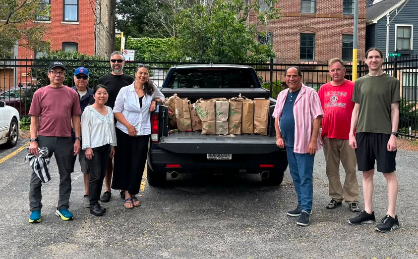 Eight people of various ages, genders, and ethnicities pose for the camera with a pickup truck full of sandwich bags. Photo is from the Midwest Buddhist Temple Facebook page.