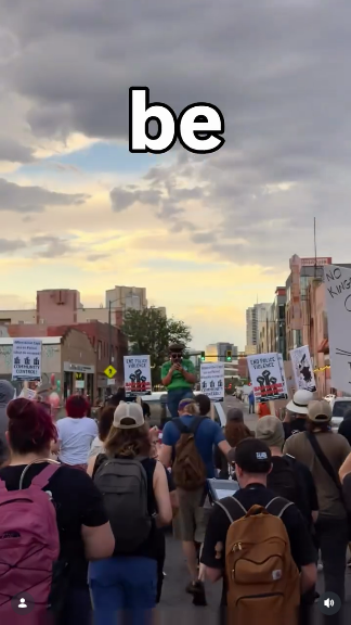 Still from the video. A crowd of people is following an activist standing in the bed of a truck through the streets of Denver.
