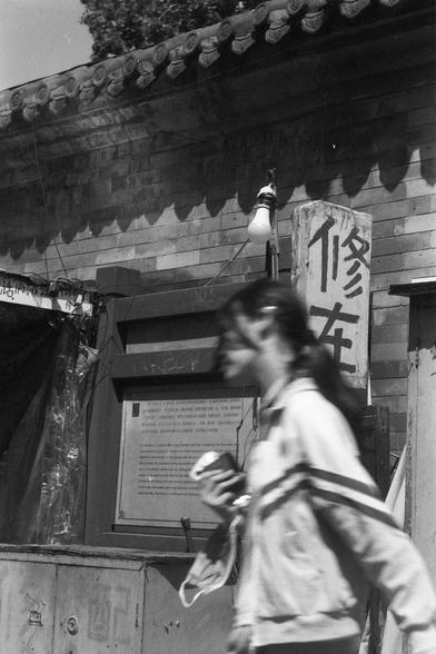 Ilford FP4 Plus 125 (FF)

English
A black-and-white photo of a person walking past a traditional building with a tiled roof and ornate eaves. A vertical sign with Chinese characters "修车" is visible on the right side of the building. The person is slightly blurred, wearing a light-colored jacket and holding things in the hand.
中文
一张黑白照片，照片中一人走过一栋传统建筑，建筑有瓦片屋顶和装饰性屋檐。建筑右侧有一个竖直的中文标志“修车”。人物略显模糊，穿着浅色外套，手上抓了东西。