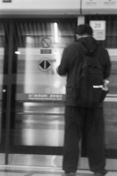 Ilford FP4 Plus 125 (FF)

English
A black-and-white image of a person standing in front of a metallic glass door with signs on it. The door has Chinese characters on it and seems to be in a subway station. The person is wearing a dark jacket and dark pants, and appears to be looking down at something.
中文
一张黑白照片，照片中一人站在一个金属门前，门上有各种标志。门上有中文字符，这似乎是一个地铁站。该人穿着深色外套和深色裤子，似乎在向下看。