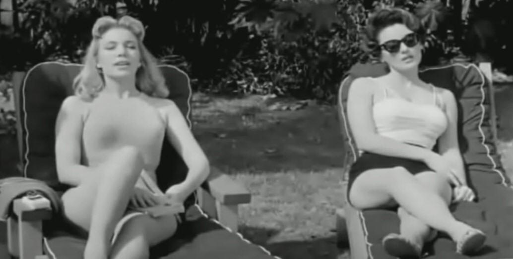 Actresses Sally Todd and Allison Hayes in swimsuits sunbathing by a pool.