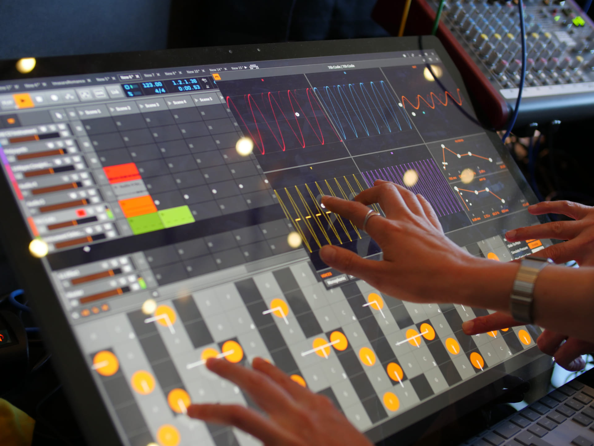 Four hands interacting with Bitwig Studio's tablet UI on a large display.