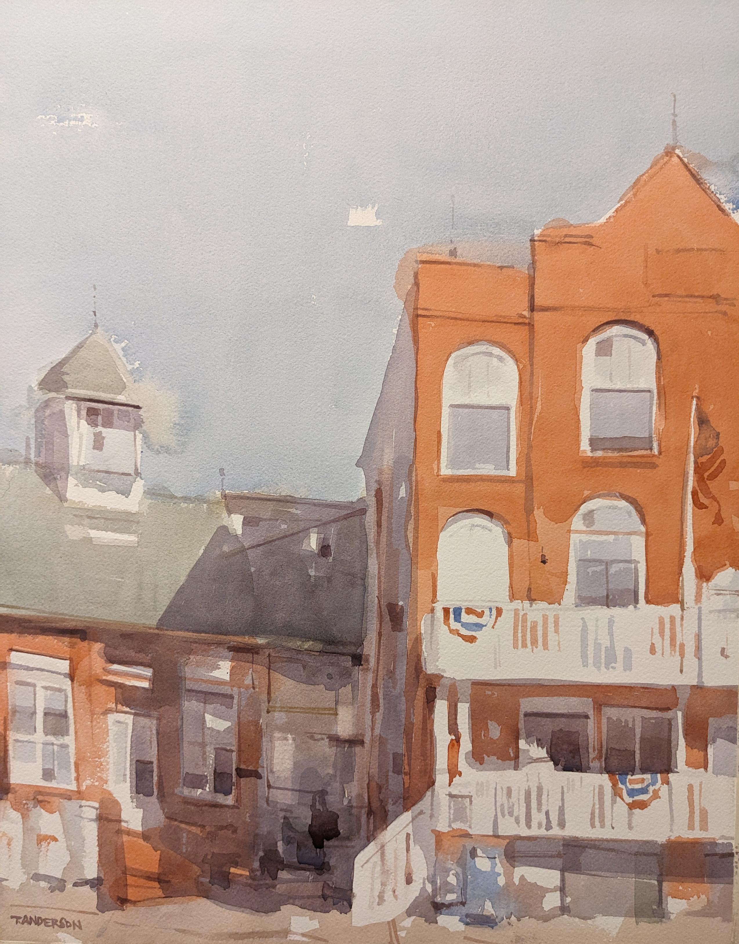 Watercolor painting of some buildings in downtown Manteo, North Carolina. A large red brick building stands to the right, dwarfing a smaller, single story brick building on the left with a grey-green asphalt roof and small widow's peak rising in the center. The large building on the right has multiple floors of arched white trim windows reflecting back the haziness of the blue Summer sky. White railings line its two lower floors with stairs to the left. The building on the left is half covered in shadow from the larger building and has several rectangular windows and entries with white trim. Buntings hang from the railings, remnants of a celebration.