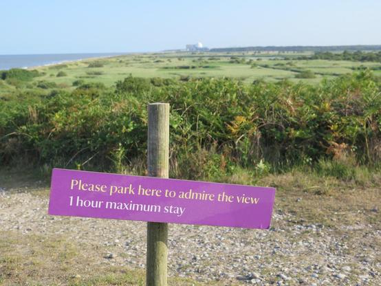 View from Dunwich Heath over part of Minsmere with Sizewell nuclear plant on the horizon.  Sign says 'Park here to admire the view.  Maximum stay 1 hour'.  Irony?
