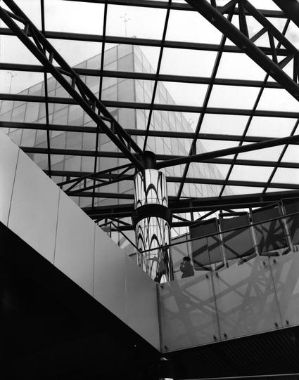 Lucky LUCKY SHD 400 (6x7)

English
A black and white photo of a outdoor mezzanine with a glass ceiling. A person stands near the metal support of the mezzanine, talking with someone on the phone. The glass ceiling has frames of beams, making an interesting pattern. Through the ceiling, one can see a modern skyscraper with a grid like pattern facade.

中文
一幅黑白照片，照片中是一个室外有玻璃顶的中层走廊。一个人在金属廊柱旁打电话。玻璃顶有金属的横梁形成的网格。透过它，可以看见一栋有网格状外墙的摩天大楼。
