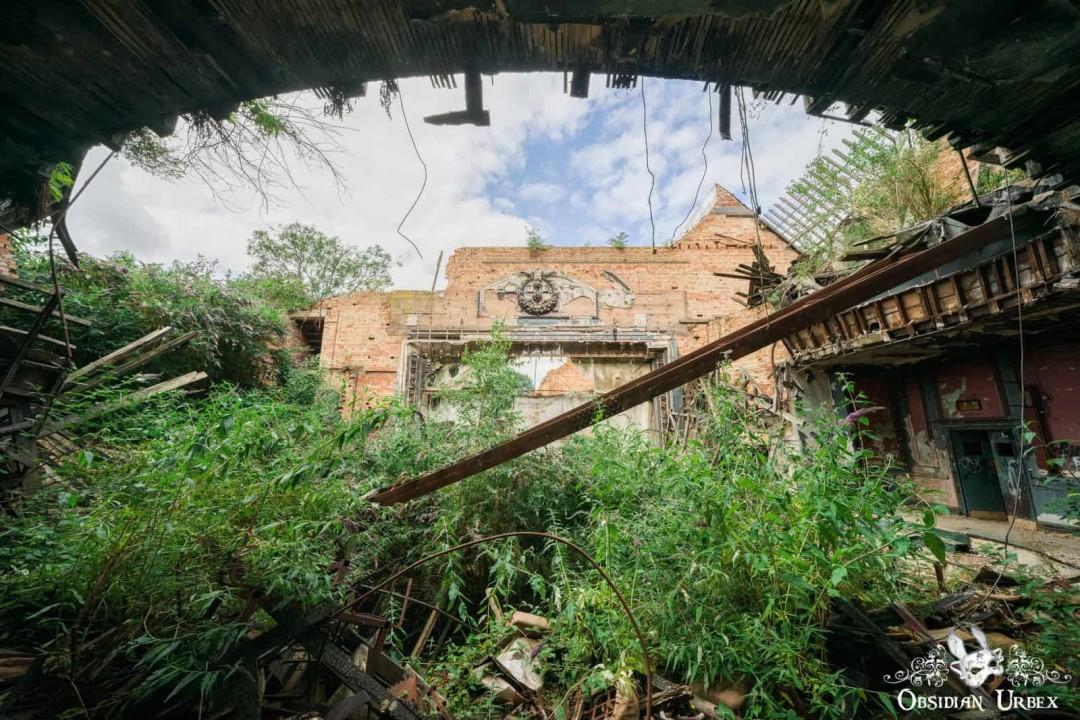 Collapsing theatre, the roof has completely fallen in and trees and bushes grow inside