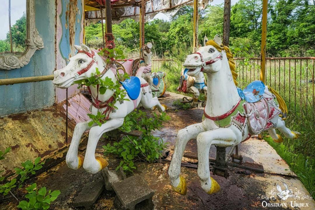 Abandoned merry go round with two horses, plants are growing on them