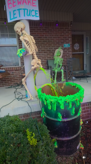 From @LeahCaitlyn12 on Ig, a life size Halloween skeleton is propped up on a column on her front porch with a sign that says "BEWARE LETTUCE" overhead. Behind it is a 50 gallon drum with green expanding foam around the top. It's full of yellow-green highlighter fluid with a small pump sending the water up through a hose on the skeleton's legs. The mouth of the hose, which is clamped to make the fluid spew out, is coming out the back of the skeleton's pelvis to mimic diarrhea. It's also holding a bowl contained scraps of green tissue paper to represent lettuce.