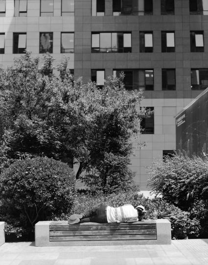 Lucky LUCKY SHD 100 (6x7)

English alt text: Black-and-white photo taken outdoors. A modern building fills the background, with many rectangular windows arranged in rows. In the foreground, a large wooden bench is centered, and a person is lying down on the bench. Dense bushes and small trees surround the bench, filling most of the lower half of the image. The person’s clothing appears light in tone, and the person is resting with their body lying horizontally on the bench.
中文 alt text： 黑白户外照片。…