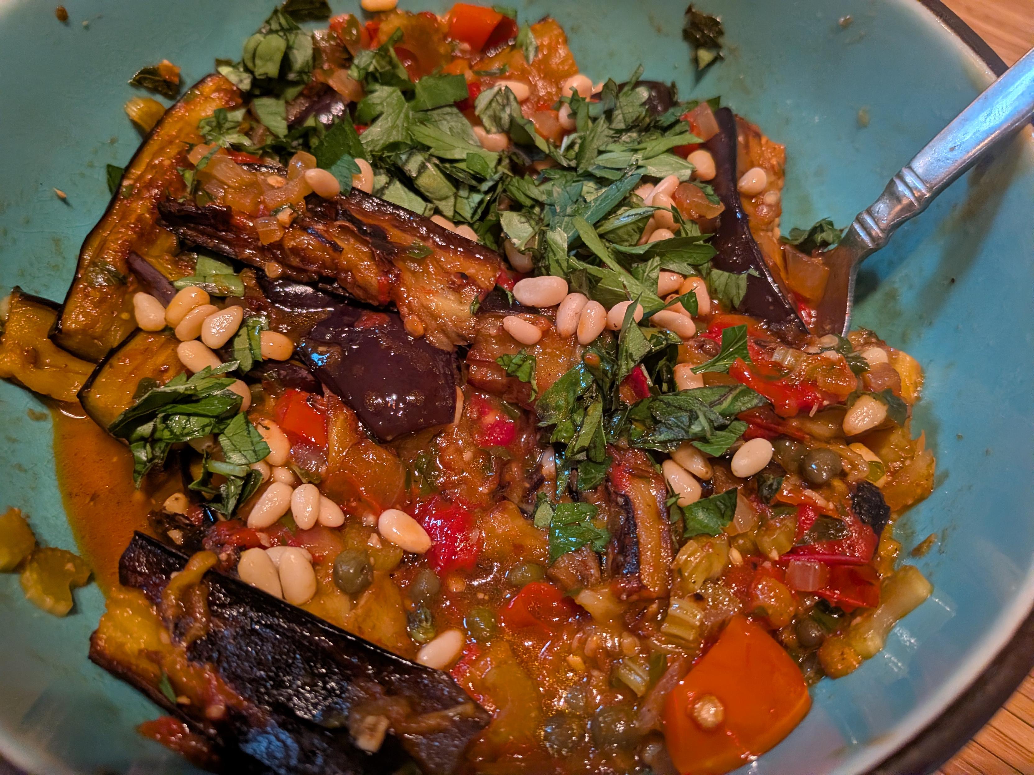 A bowl of stewed eggplant, tomatoes, pine nuts, and herbs