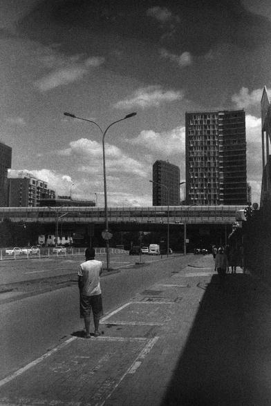 ERA 100 (FF)

English
A black-and-white photograph of a city street with a pedestrian standing on the sidewalk. The street is lined with tall buildings, streetlights, and a few vehicles. The sky is partly cloudy, and the image captures a sense of urban life with people and infrastructure.
中文
一张黑白照片，拍摄的是一条城市街道，人行道上站着一个行人。街道两侧是高楼大厦、路灯和几辆车。天空部分多云，图片展现了城市生活的景象，包括行人和基础设施。