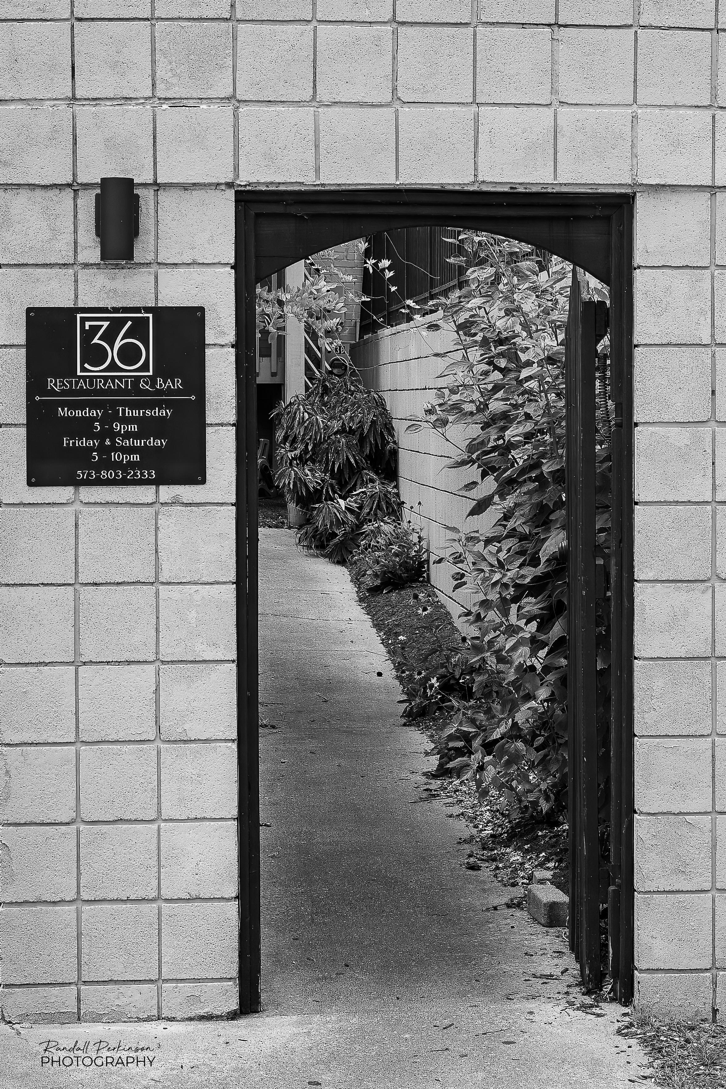 A concrete block wall with a black metal gate at the open air entrance into a restaurant and bar called 36.