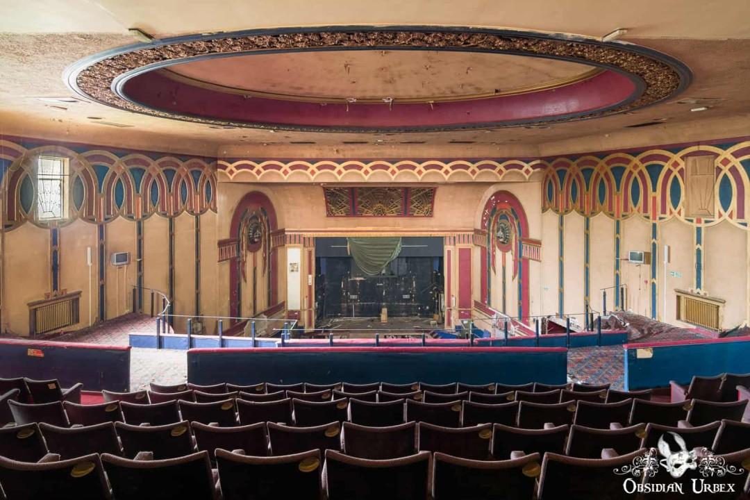 Interior of the abandoned Royalty Cinema in England, featuring rows of empty seats and an ornate stage. The grand, decaying theatre is