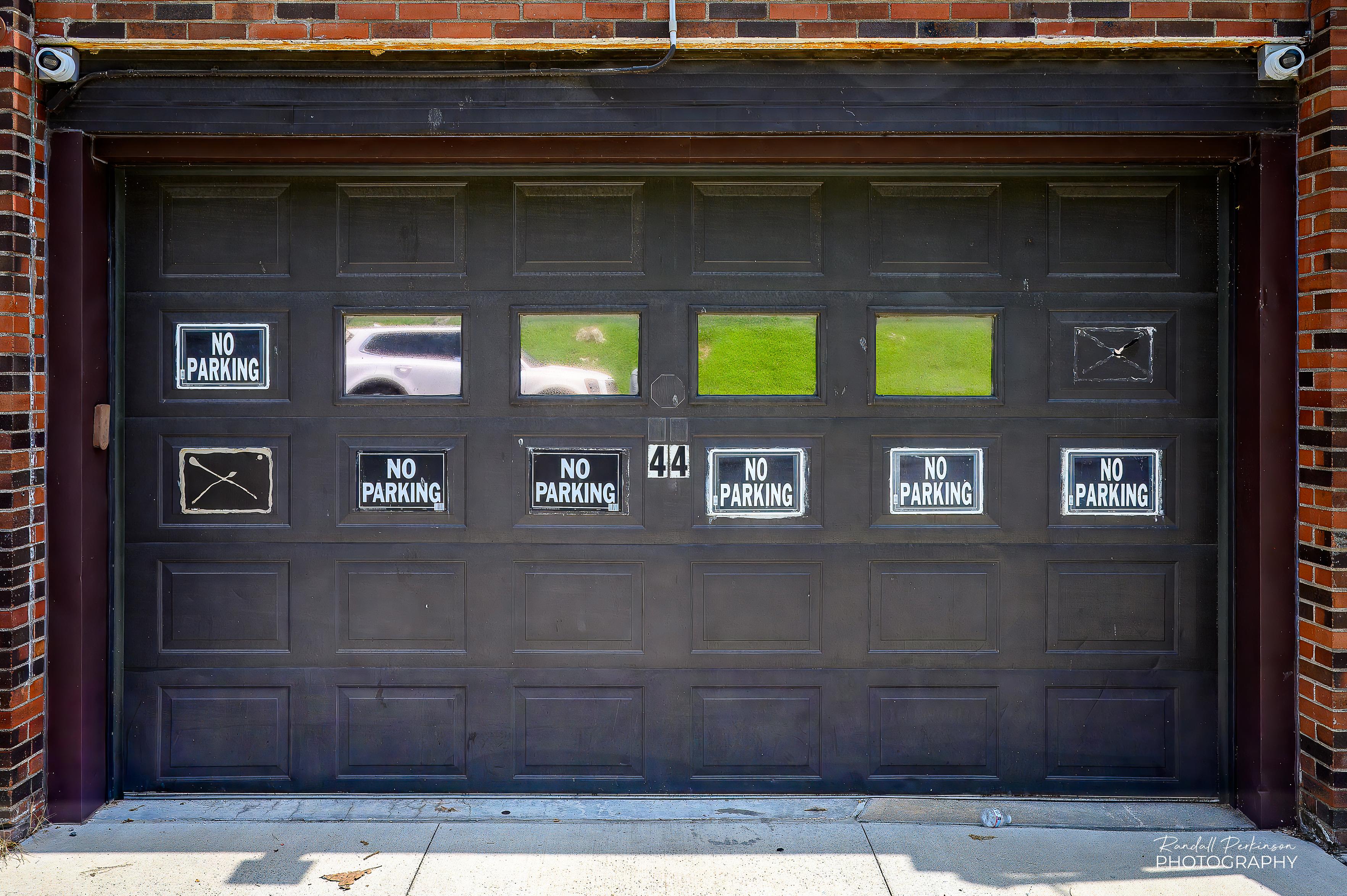 A garage in a brick building has 6 separate "NO PARKING" signs along with 2 spots where it looks like additional signs used to be located.  It's almost like they're daring people to park in front of the garage. :-)