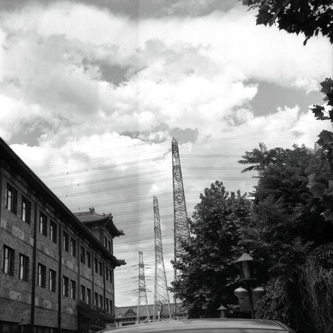 Lucky LUCKY SHD 100 (6x6)

English
A black-and-white photograph featuring a traditional multi-story brick building on the left side of the frame. The building has ornate details and a tiled roof. In the background, there are tall metal lattice towers, likely electrical pylons, rising into a cloudy sky. Trees and foliage partially obscure the view of the towers and the building.
中文
一张黑白照片，左侧是一栋传统的多层砖结构建筑，建筑上有装饰性细节和瓦片屋顶。背景中有高大的金属格子塔，可能是电力铁塔，耸入多云的天空。树木和植被部分遮挡了塔和建筑的视线。