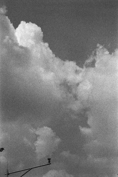 Ilford HP5 Plus 400 (FF)

English
A black-and-white photograph of a sky filled with large, fluffy cumulus clouds. The clouds dominate the frame, creating a dramatic and textured appearance. In the lower portion of the image, parts of streetlights or poles are faintly visible against the bright sky.
中文
一张黑白照片，天空中充满了大块蓬松的积云。云朵占据了画面的大部分，营造出一种戏剧性的质感。在图像的下方部分，可以隐约看到路灯或杆子的轮廓，映衬在明亮的天空下。