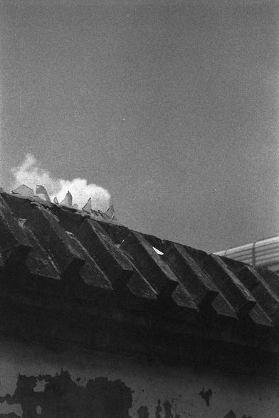 Ilford HP5 Plus 400 (FF)

English
A black-and-white photograph capturing the wall of a building. The wall is composed of dark, weathered shingles, with some areas showing signs of wear and peeling paint. At the peak of the wall, there are pointed, broken glass spikes. The sky above is clear, with a hint of clouds rising from behind the roof.
中文
一张黑白照片，拍摄的是一栋建筑的墙壁。墙壁由深色、风化的木瓦组成，部分区域显示出磨损和油漆剥落的迹象。在墙的顶部，有尖状的碎玻璃。上方的天空晴朗，后方有云朵升起。