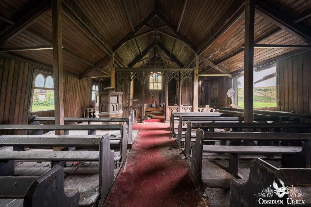 The decaying interior of the abandoned Iron Church, featuring wooden pews and a faded red carpet leading to a carved altar.