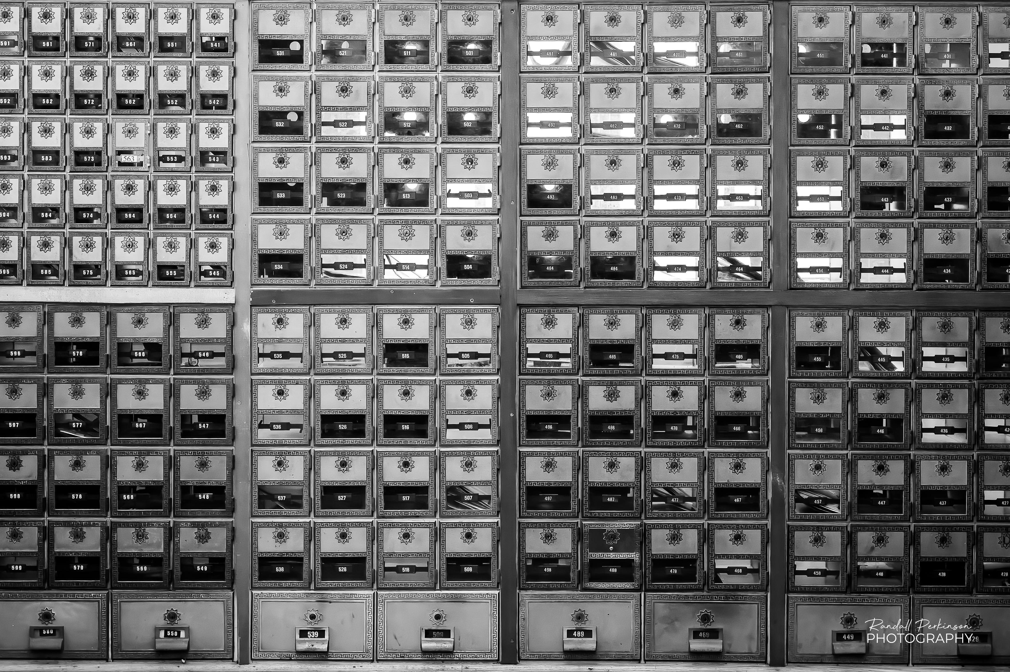 a view of several dozen post office boxes lining the wall of a post office.