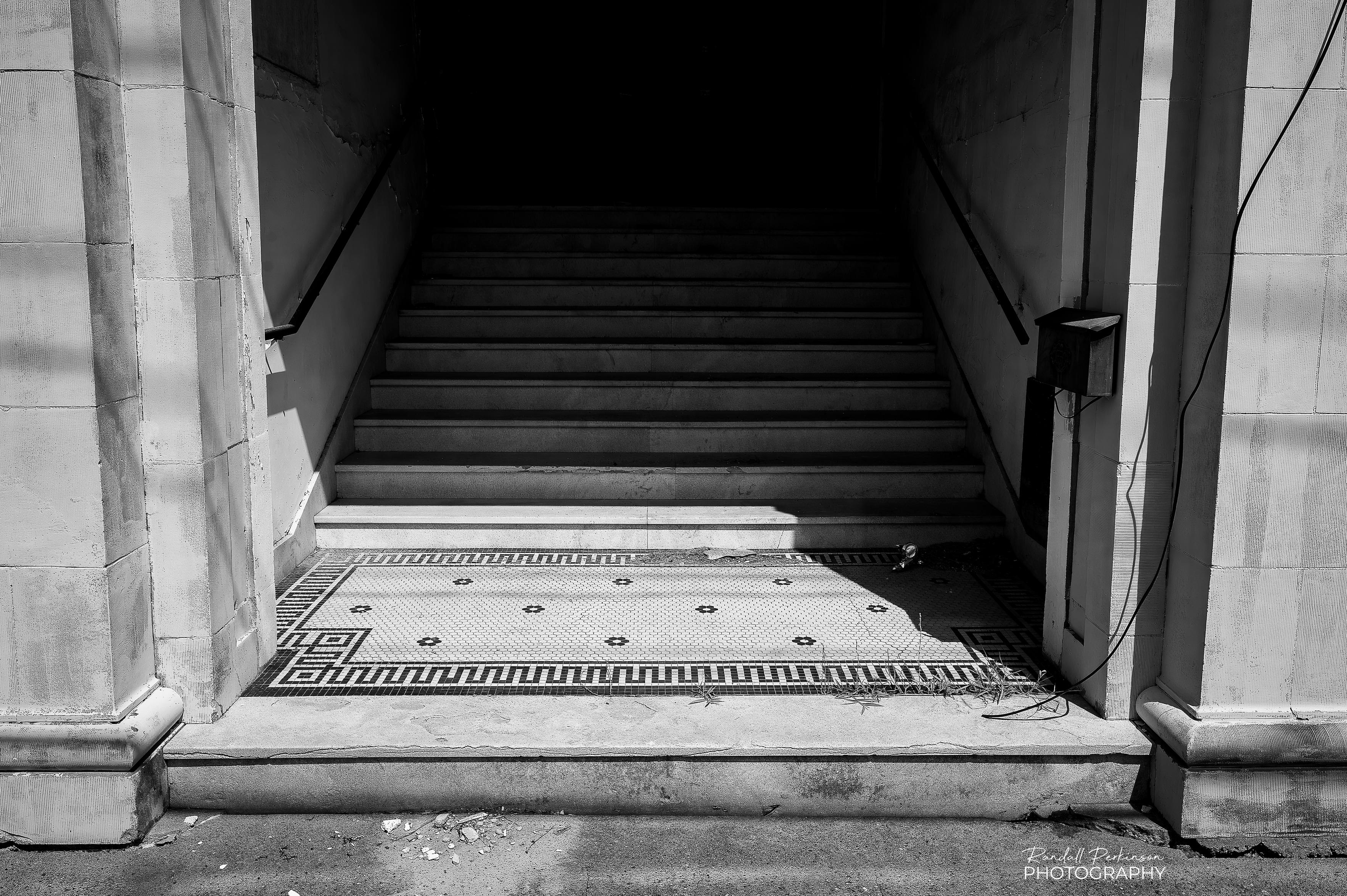 An entryway into a large stone building has stairs leading into darkness.