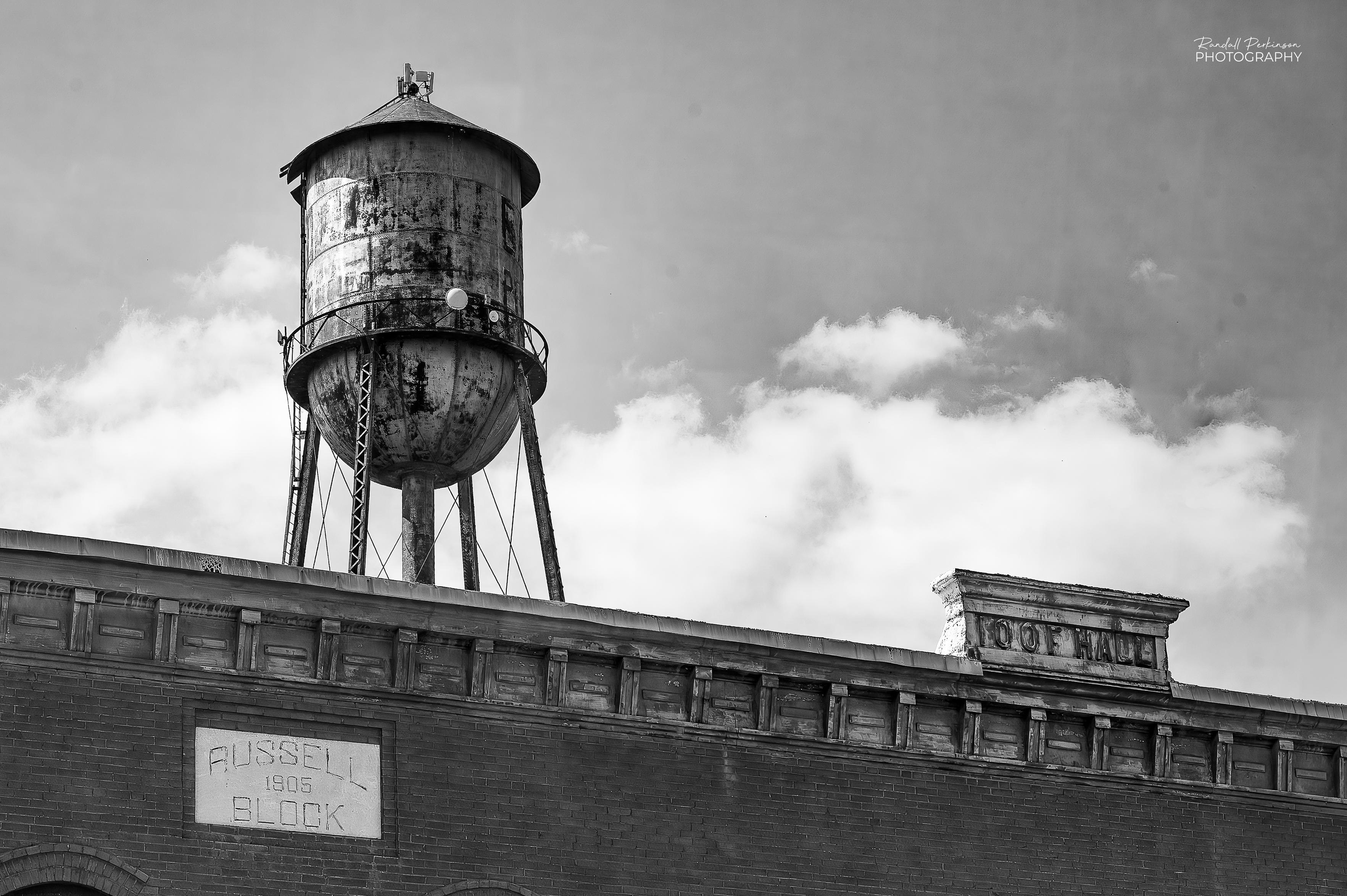 A view of the top of a building with text reading "Russell Block" and "IOOF HALL", with an old municipal water tower rising behind it.