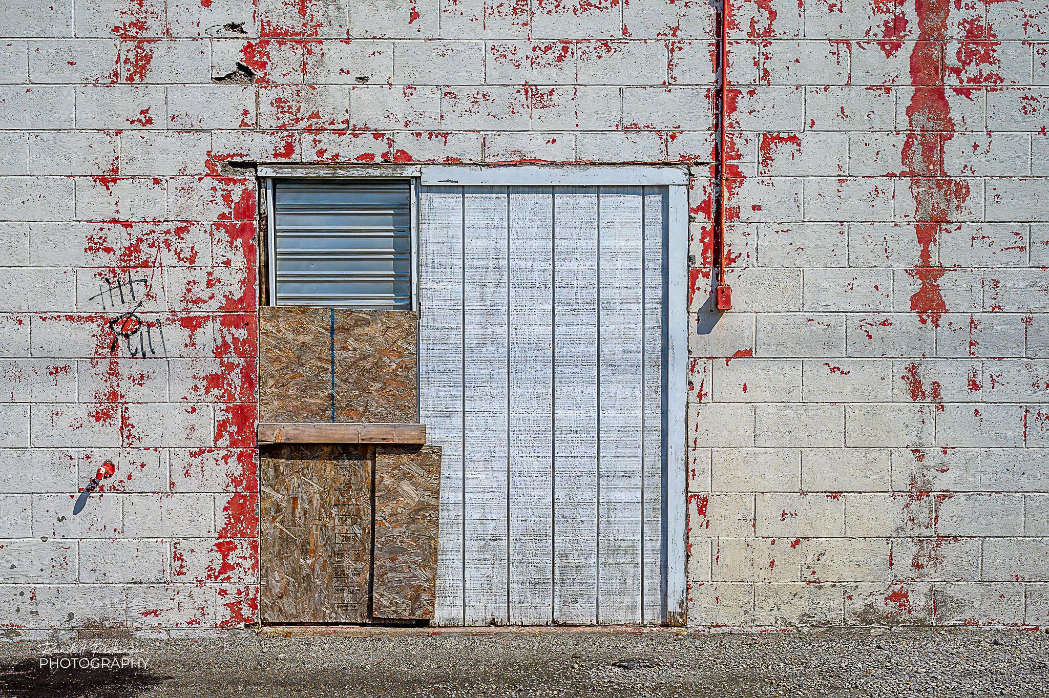 A concrete block building with a boarded up entrance that has an exhaust vent.