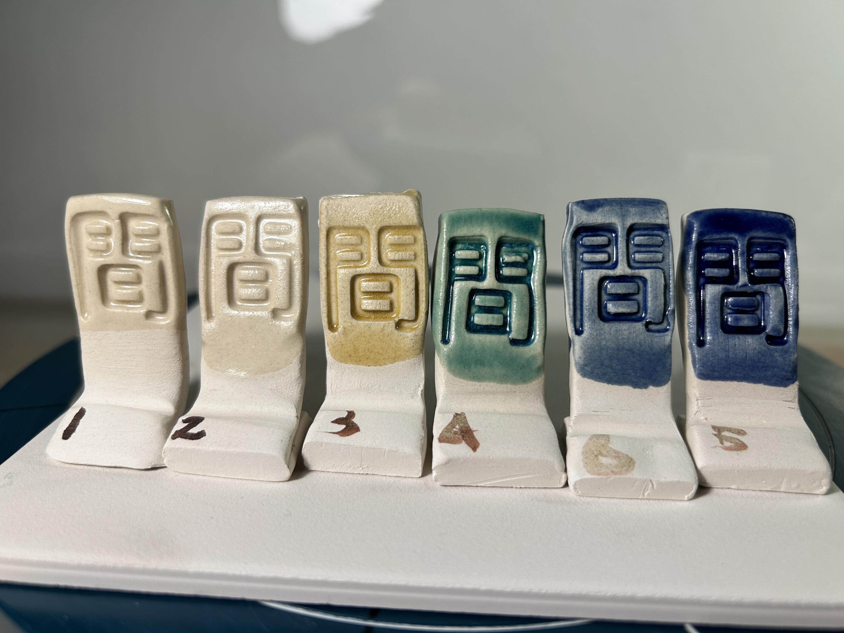 Test tiles with fired glaze lined up in a row showing the single coat of glaze fronts.